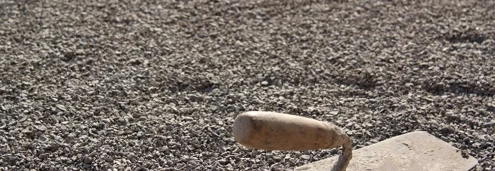 Eine Maurerkelle liegt auf einem Schotterbett.